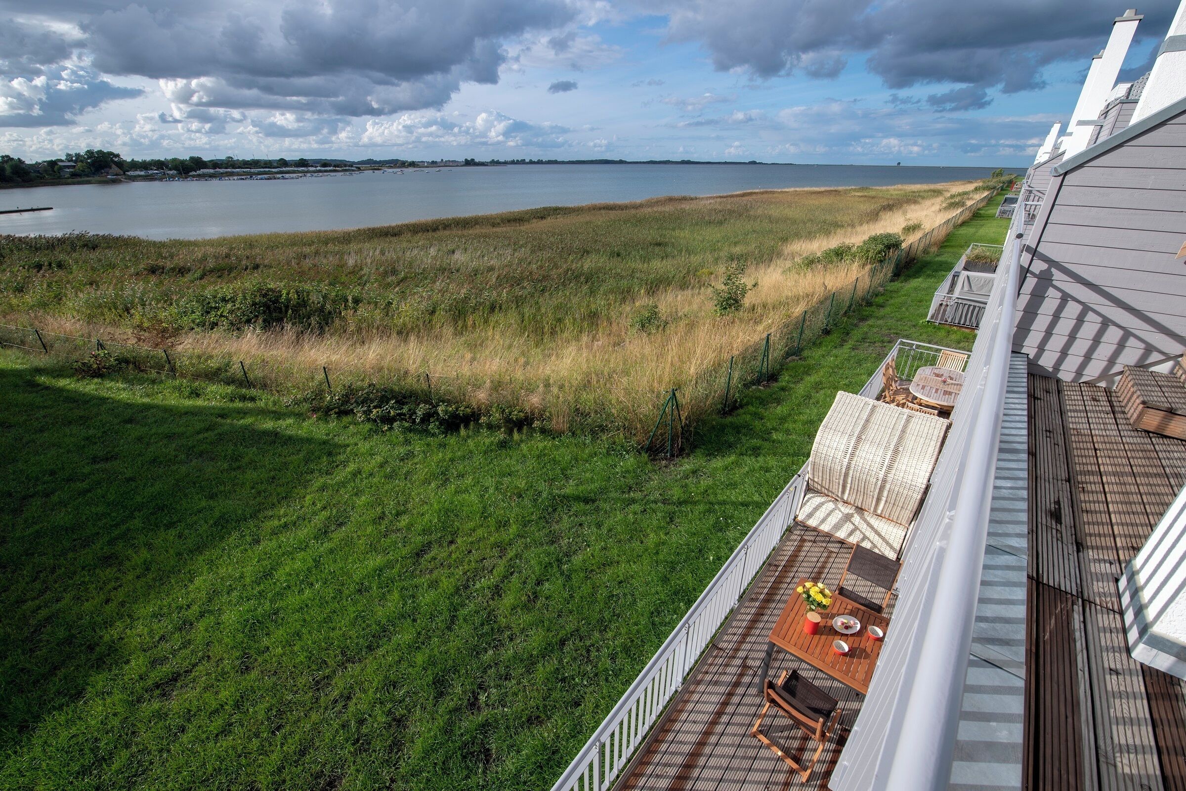 A view from a balcony overlooking a grassy area with a body of water and a distant shoreline.