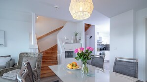 A modern dining area with a glass table, wicker chairs, a vase of flowers, and a kitchen in the background. - Silbermöwe - Rooftop Terrace with Panoramic Views, First Row Waterfront, Firepla (Olpenitz)