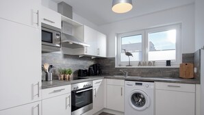 A modern kitchen with white cabinetry, a built-in oven, a microwave, a dishwasher, and a window with a view. - Silbermöwe - Rooftop Terrace with Panoramic Views, First Row Waterfront, Firepla (Olpenitz)