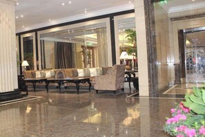 A lobby with a seating area, a reception desk, and a large mirror reflecting the interior. - Joyful Hotel (Yueqing)