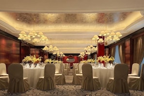 A banquet hall with round tables, chandeliers, and floral centerpieces.