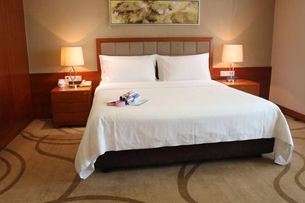 A hotel room with a large bed, two bedside tables with lamps, a headboard, and a carpeted floor.