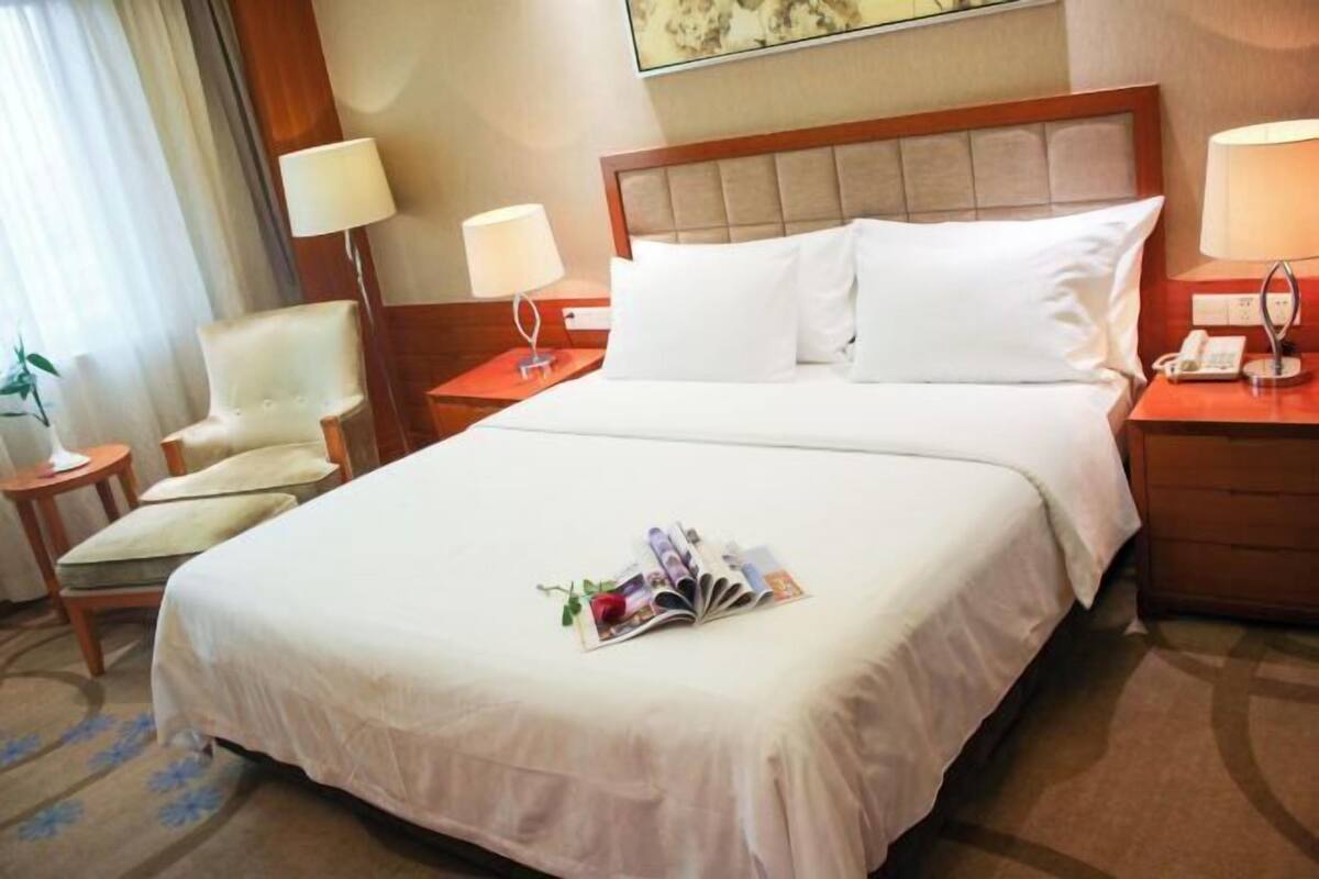 A hotel room with a large bed, two bedside tables with lamps, a chair, and a small table with a magazine.