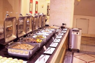 Un bufé con varias estaciones de comida, que incluye bandejas de frutas, verduras y diversos platos.