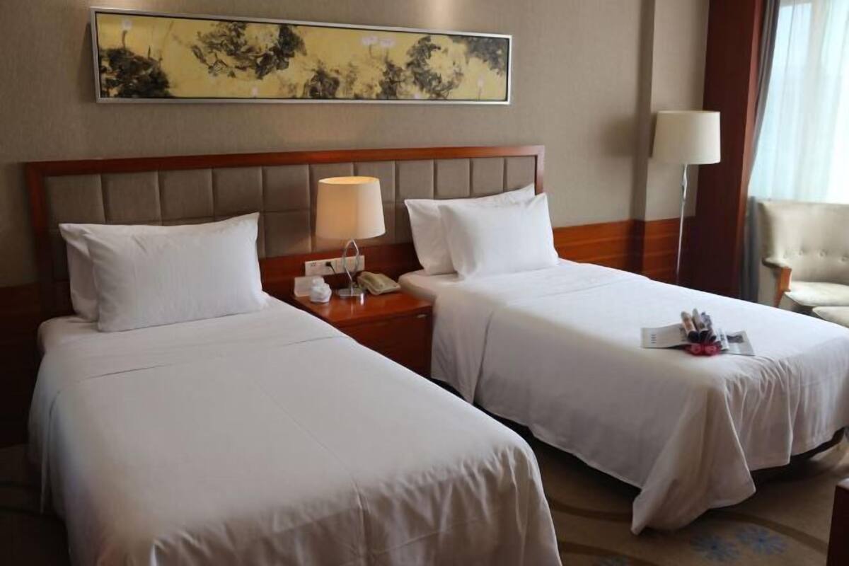 A hotel room with two beds, a nightstand with a lamp, a telephone, and a painting on the wall.