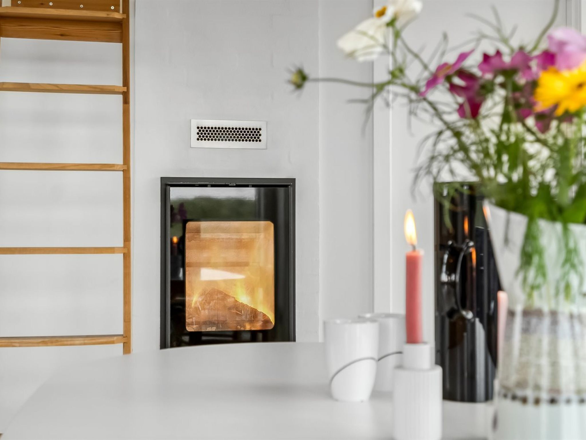 Une cheminée moderne dotée d’une porte en verre, un mur blanc et une étagère en bois sur le côté gauche.