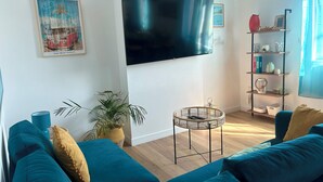 Een woonkamer met smaragdgroene banken, een flatscreen televisie, een boekenkast en een plant in pot.