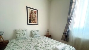 Een netjes opgemaakt bed met een sprei met bladmotief, een lijstwerk aan de muur en een nachtkastje met een lamp.