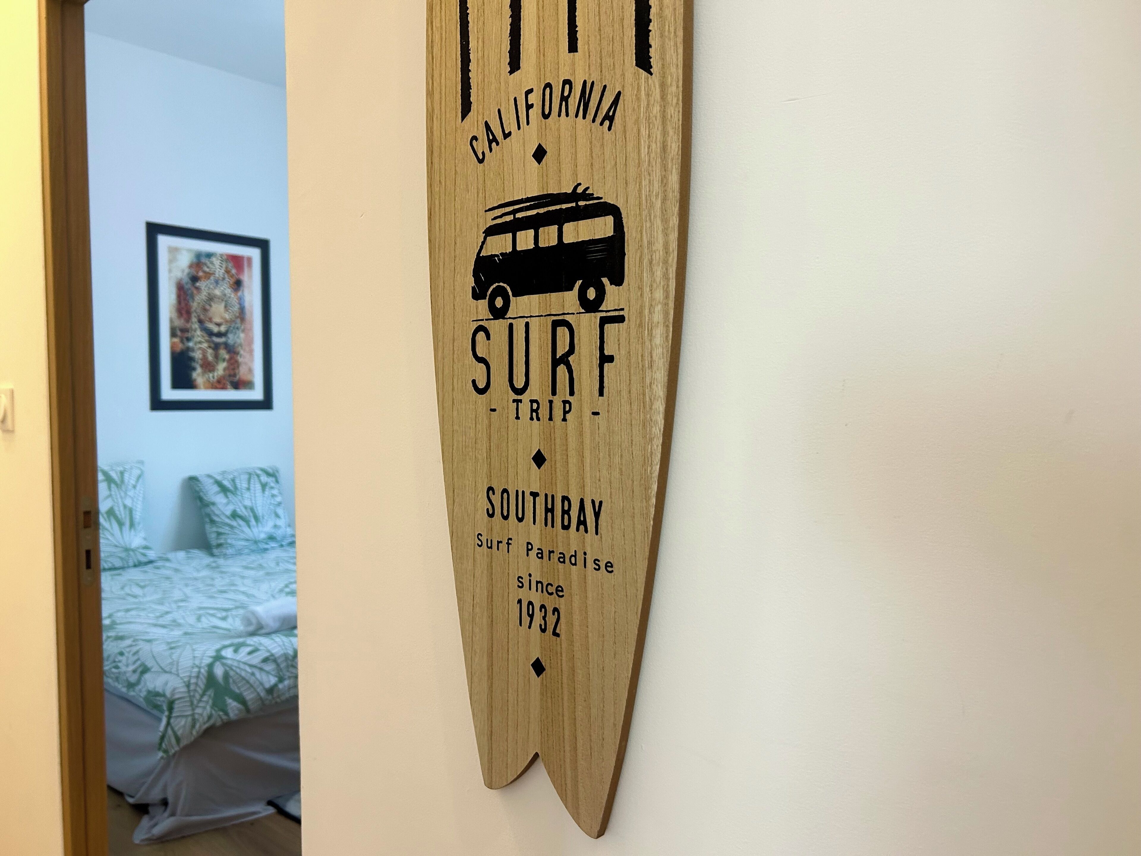 Ein hölzernes Schild mit Text und einer Busgrafik, in einem Zimmer mit einem Bett und einem gerahmten Bild an der Wand.