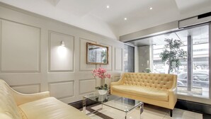Een moderne lobby met een beige bank, een glazen salontafel en een grote spiegel.