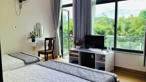 Une chambre d’hôtel moderne dotée d’un grand lit, d’une télévision et d’un balcon offrant une vue sur la verdure.