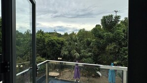 Un balcon doté d’une balustrade en verre, offrant une vue sur une piscine et une végétation luxuriante.
