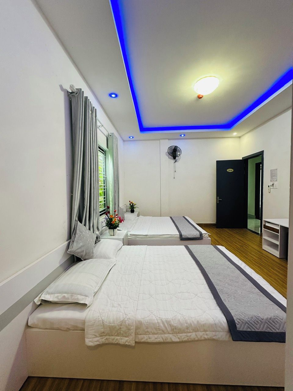 Une chambre d’hôtel moderne avec deux lits, un ventilateur de plafond et un petit bureau.
