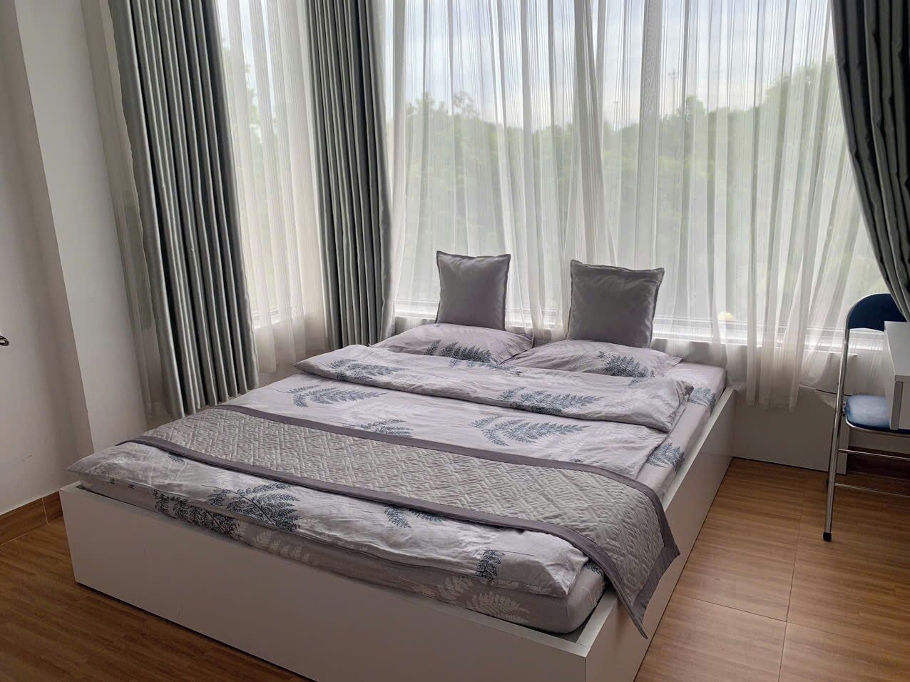 A modern bedroom with a large bed, sheer curtains, and a view of greenery outside.