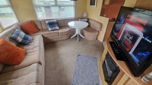 Un interno camper accogliente con un divano, un piccolo tavolino rotondo, un televisore e un angolo cottura.