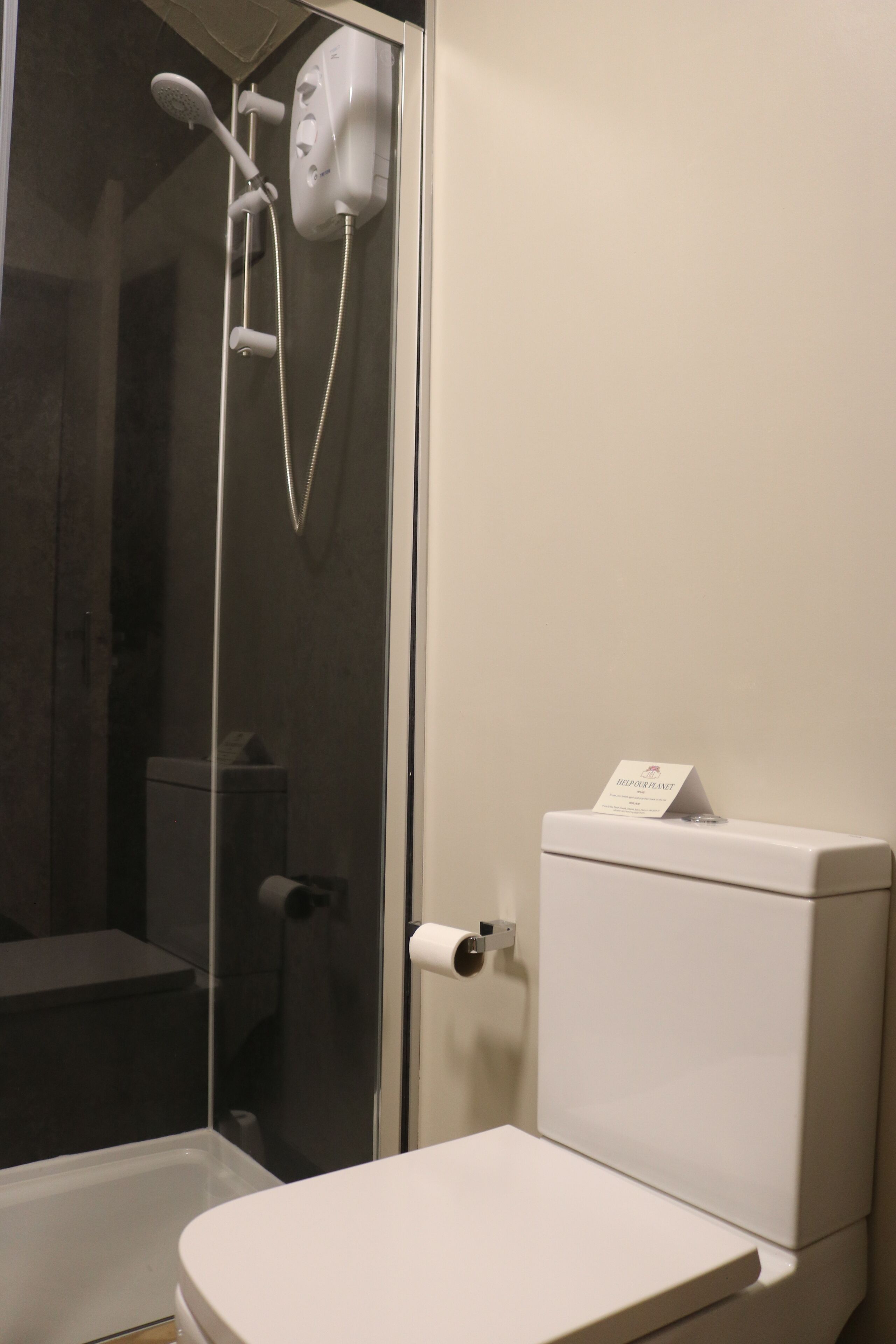 Un baño con inodoro, cabina de ducha de vidrio y un dispensador de papel higiénico blanco.
