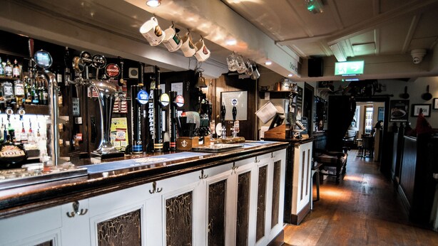 A bar with a long counter, multiple taps, and a variety of bottles. - Black Dog Inn (Bolton)