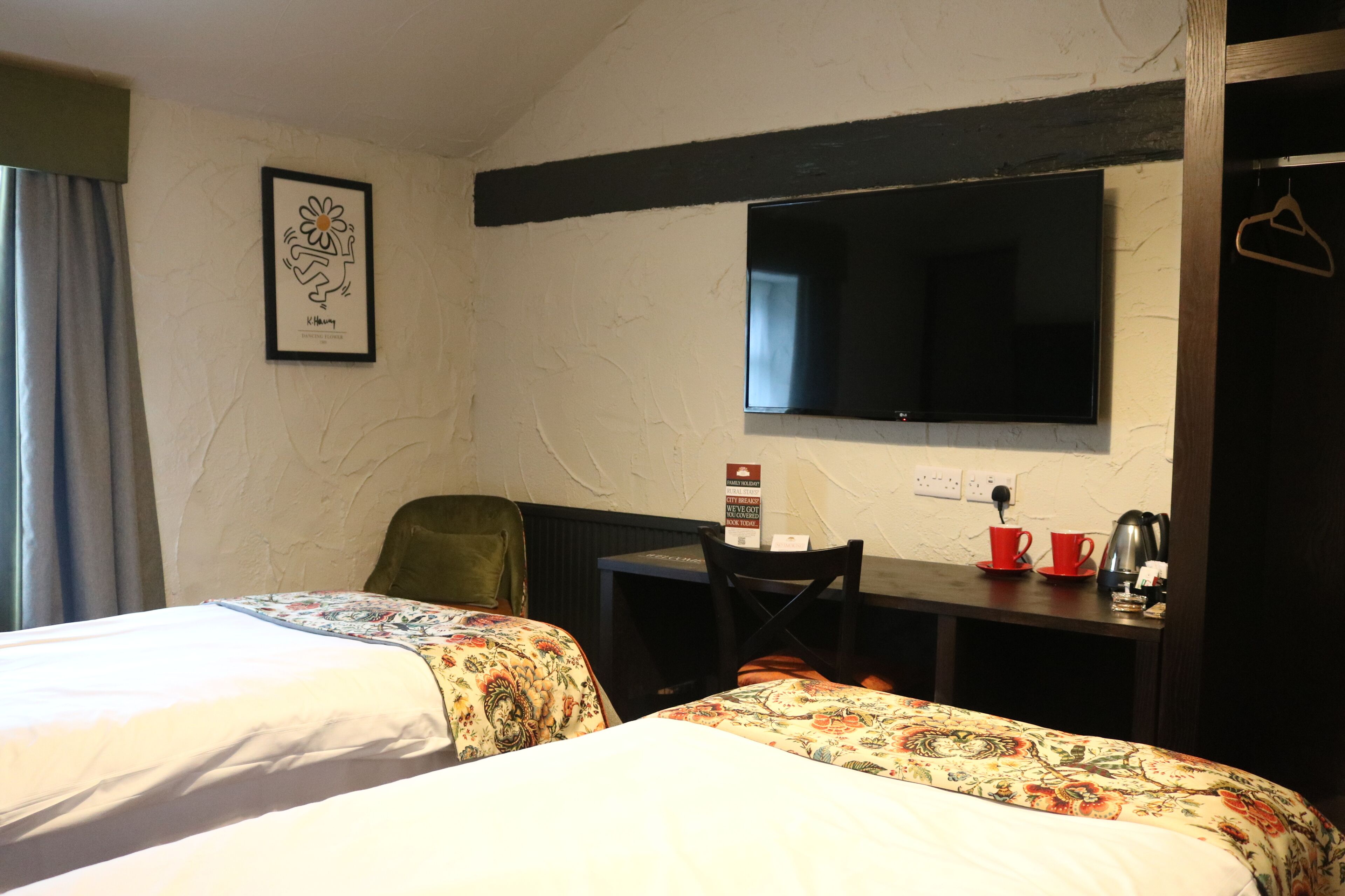A hotel room with two beds, a desk, a chair, a TV, and a coat rack.