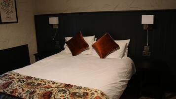 Un lit bien fait, recouvert d’une couvre-lit à motifs floraux, avec deux oreillers marron et une tête de lit agrémentée de lampes fixées au mur.