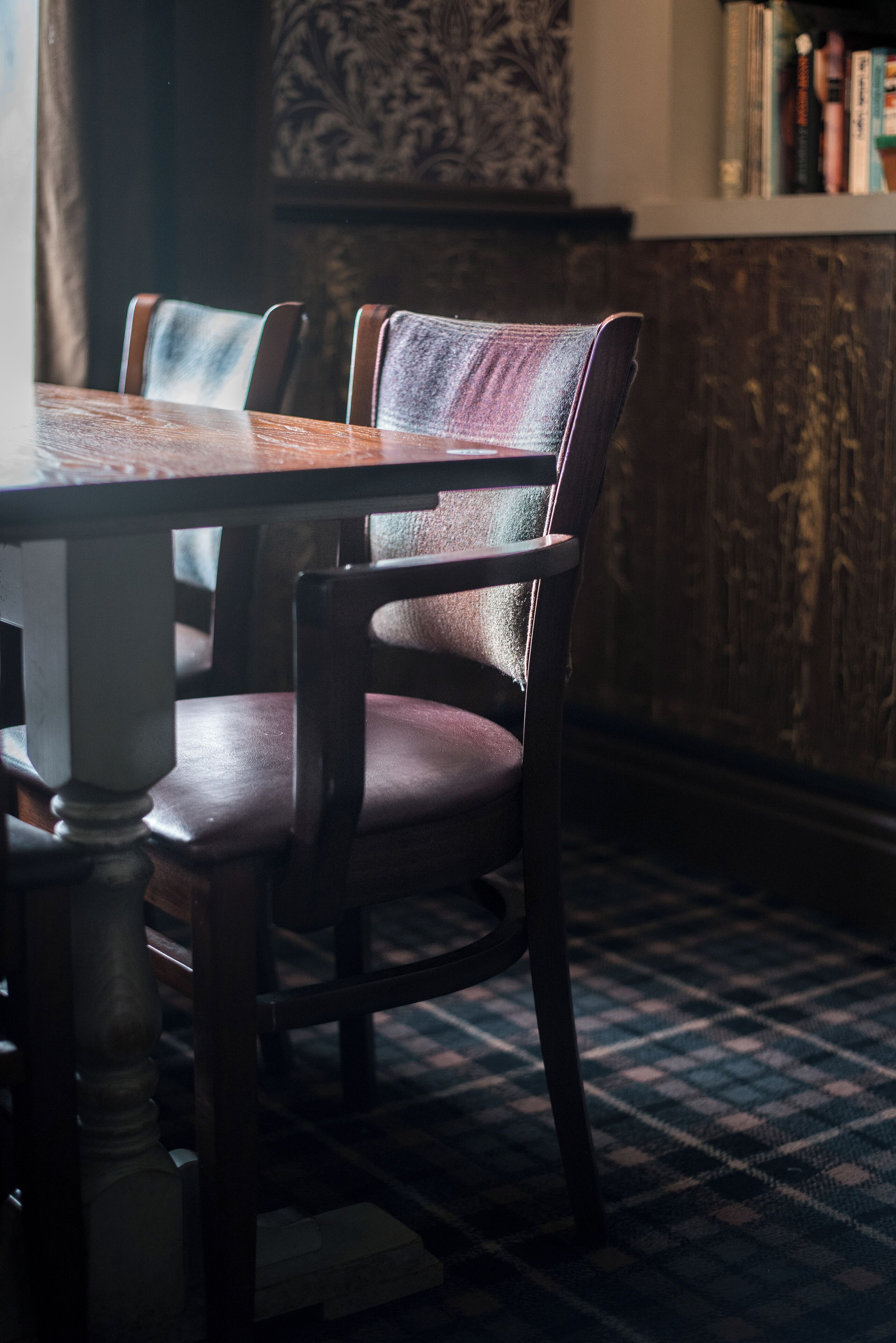 Un comedor con una mesa y sillas de madera, alfombra estampada y una estantería al fondo.