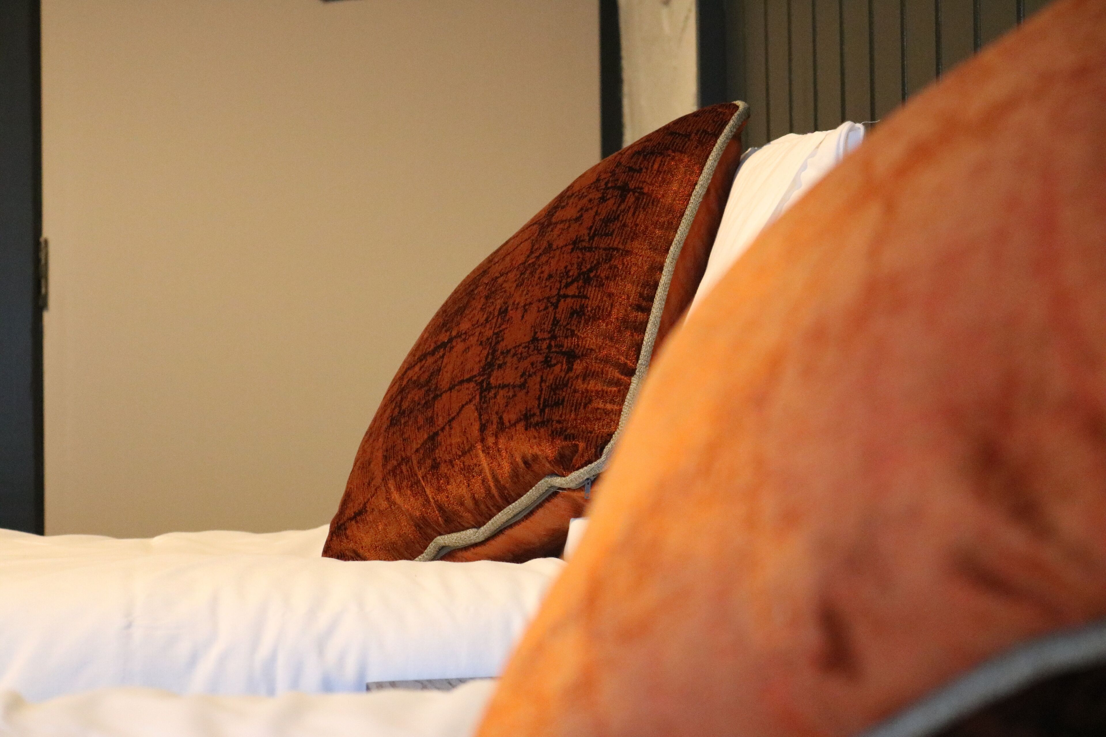 Una cama con ropa de cama blanca y almohada marrón.