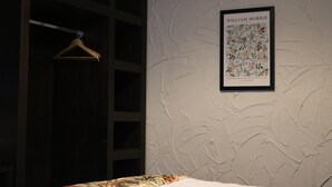 A framed artwork on a textured wall, a wooden hanger, and a bed with a patterned bedspread. - Black Dog Inn (Bolton)