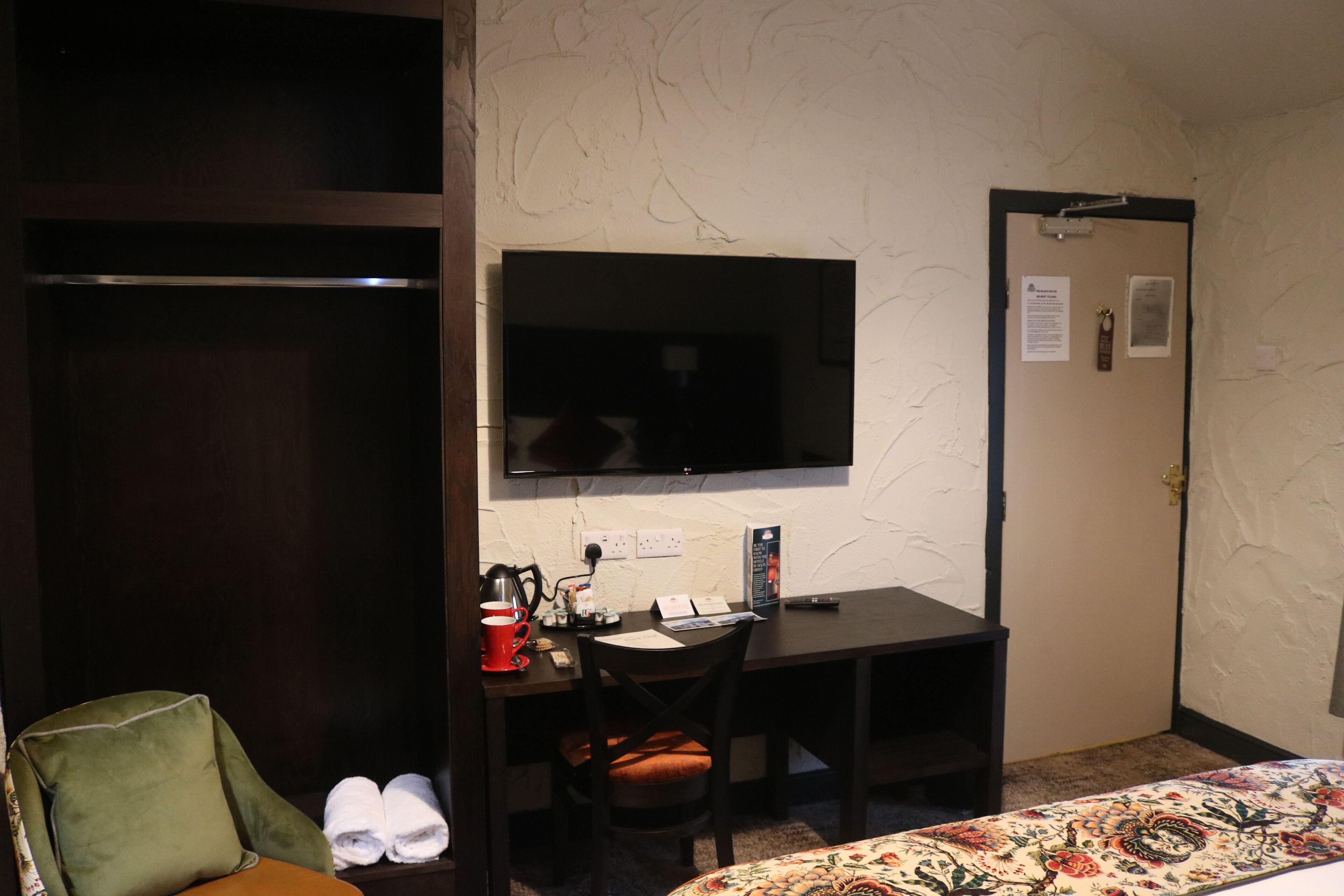 A hotel room with a bed, a desk with a chair, a television, and a wardrobe.