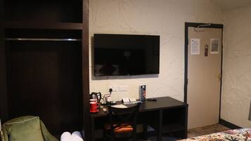 A hotel room with a bed, a desk with a chair, a television, and a wardrobe.