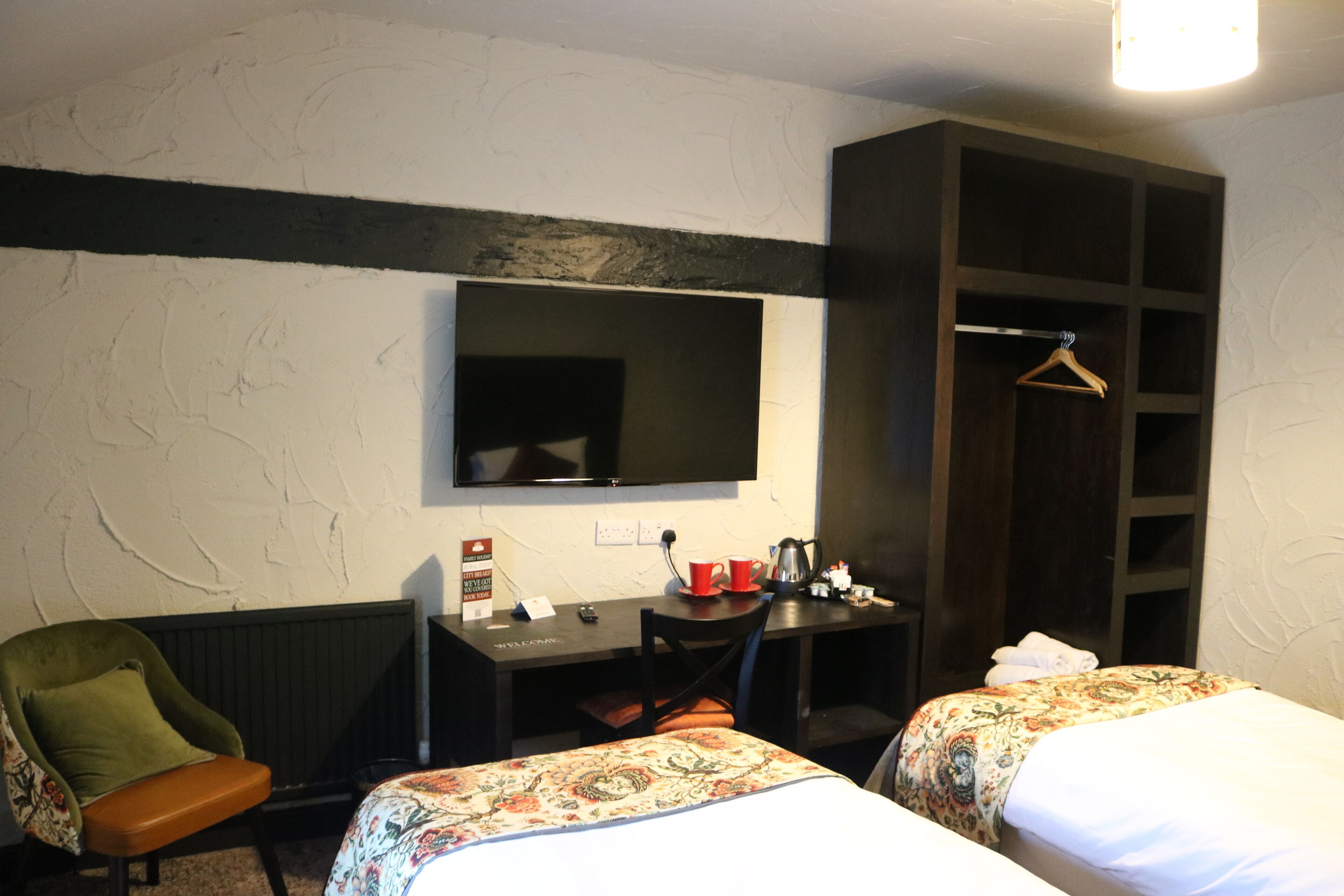 A hotel room with two beds, a desk, a chair, a television, and a wardrobe.