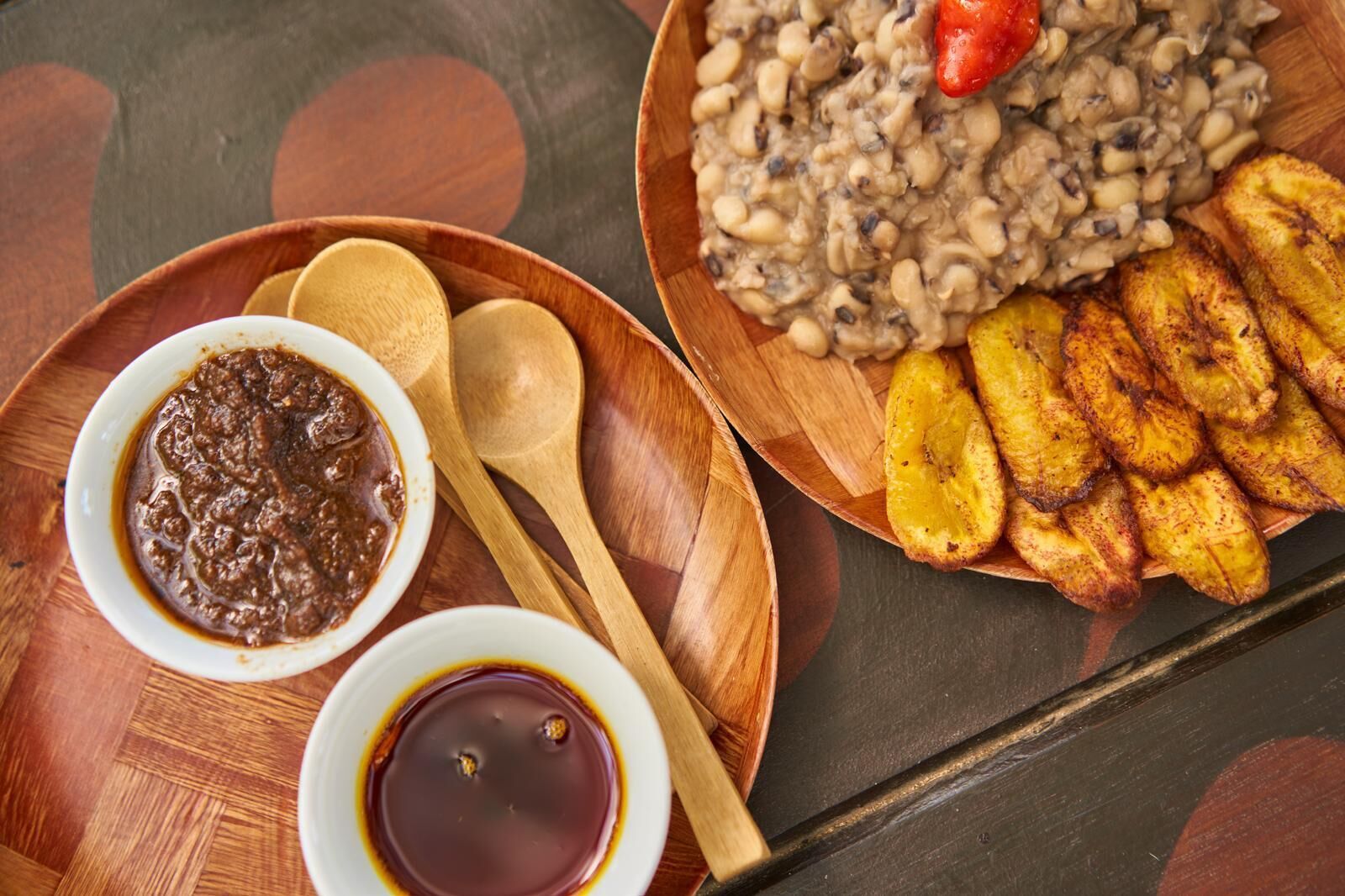 A wooden table with a plate of plantains, a bowl of beans, and a bowl of sauce.