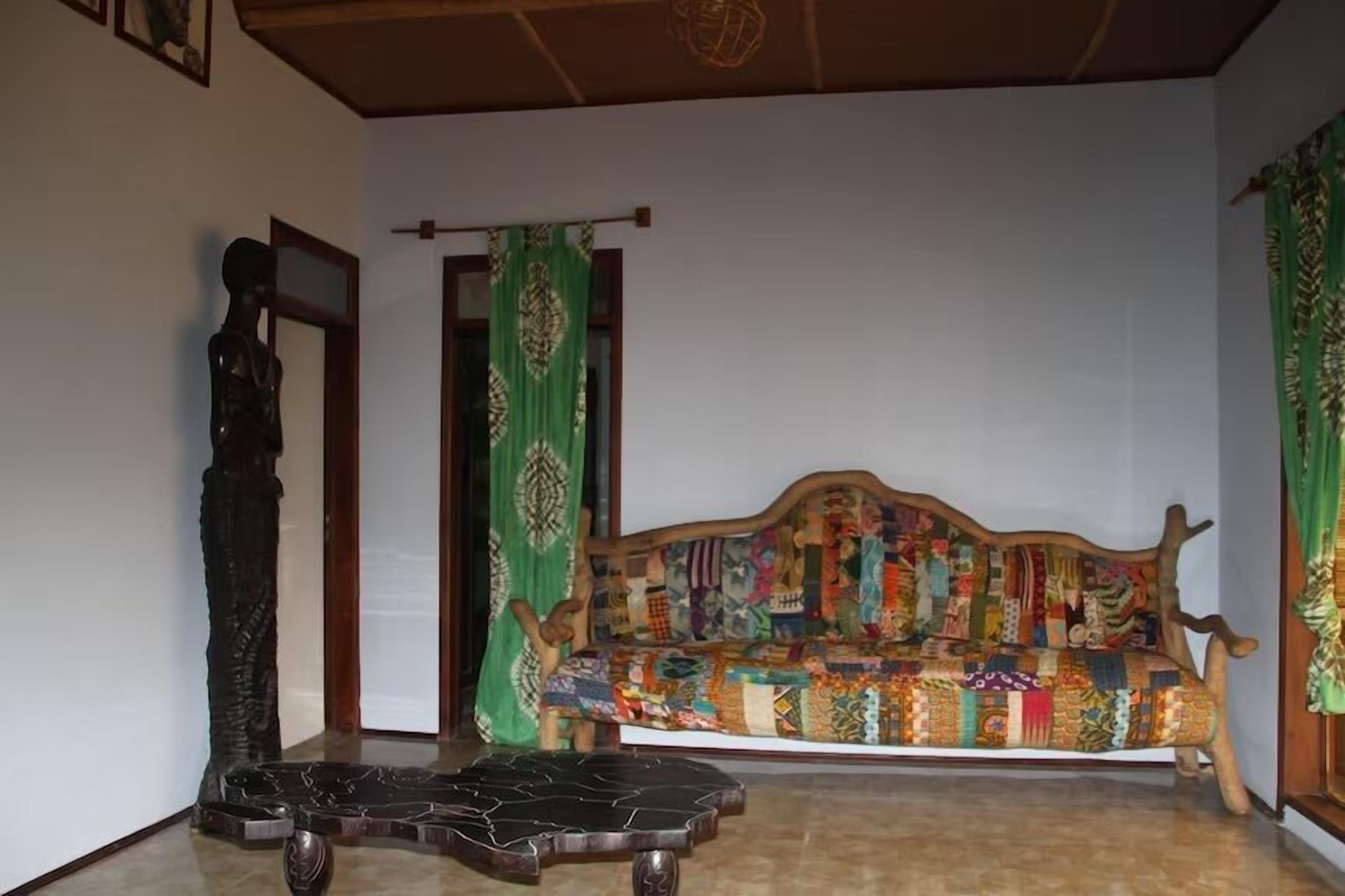Una habitación con un banco de madera cubierto de tela colorida, suelo oscuro y cortinas verdes.