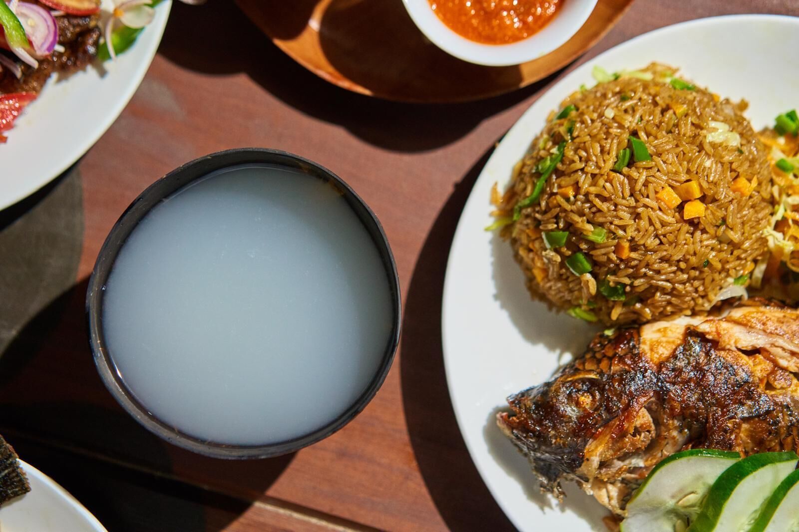 A table with a plate of fried rice, a bowl of soup, and a grilled fish.