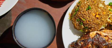 A table with a plate of fried rice, a bowl of soup, and a grilled fish.