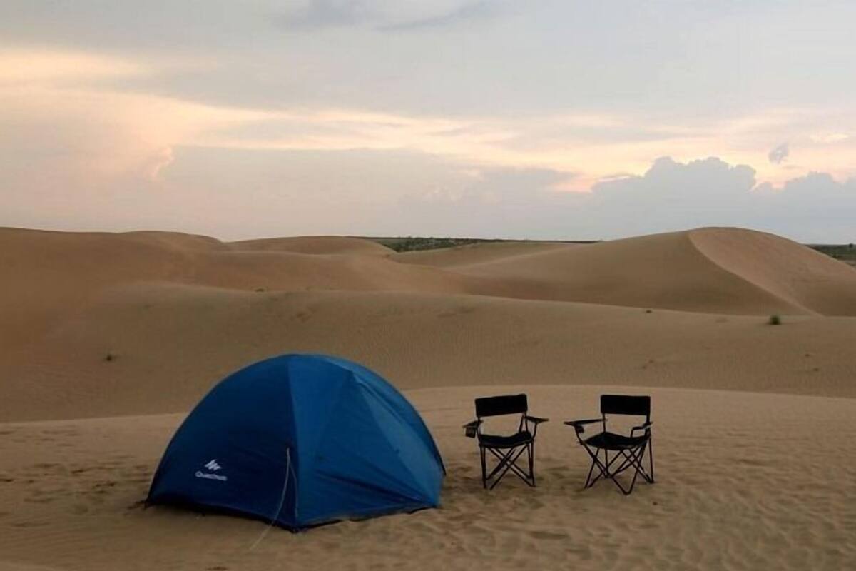 Une tente bleue avec deux chaises noires, le tout situé dans un décor désertique.