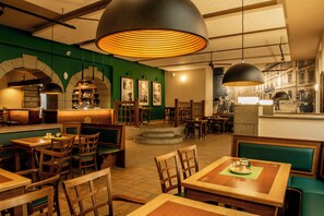 Ein Restaurantinneres mit Holztischen und -sitzecken, grünen Polstersesseln und einer Bar mit Flaschenregalen.