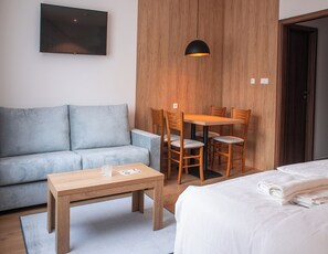 A modern hotel room with a sofa, a wooden dining table with chairs, a small wooden table, and a bed with a white duvet. - Beseda Accomodation (Ceské Budejovice)