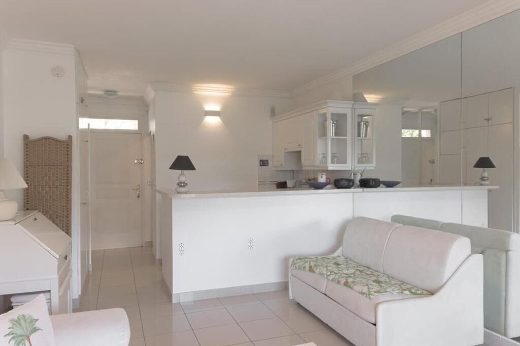 Una sala de estar moderna y bien iluminada con un sofá, una mesita y una zona de cocina con armarios y una encimera.