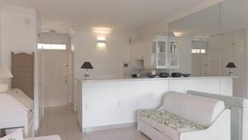 Una sala de estar moderna y bien iluminada con un sofá, una mesita y una zona de cocina con armarios y una encimera.