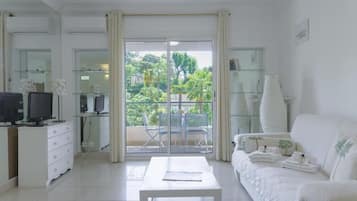 Una sala de estar moderna con un sofá blanco, una mesita de centro, un televisor y un balcón con puertas de cristal.