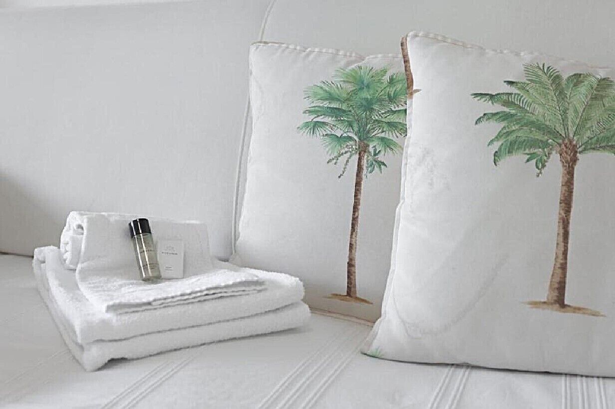 Una cama bien hecha con sábanas blancas, una toalla doblada y un frasco de loción.