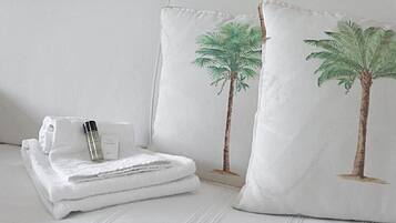 Una cama bien hecha con sábanas blancas, una toalla doblada y un frasco de loción.