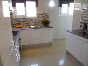 A modern kitchen with white cabinets, a stainless steel sink, and a tiled backsplash. - Penthouse Apartment in the Heart of Sitges (Sitges)