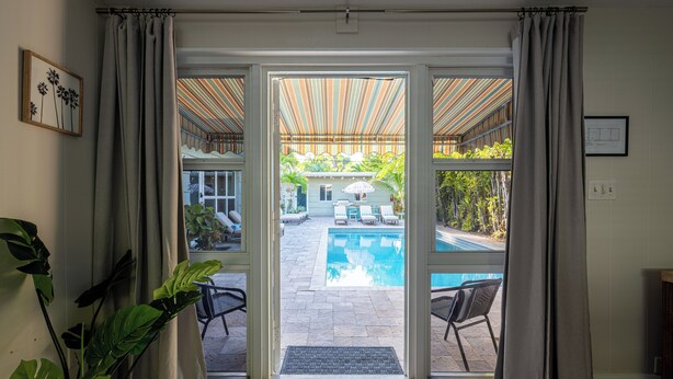 A view from inside a room to an outdoor swimming pool area with a covered patio and lounge chairs. - BRIGHT Fort Lauderdale Tropical Retreat (Fort Lauderdale)