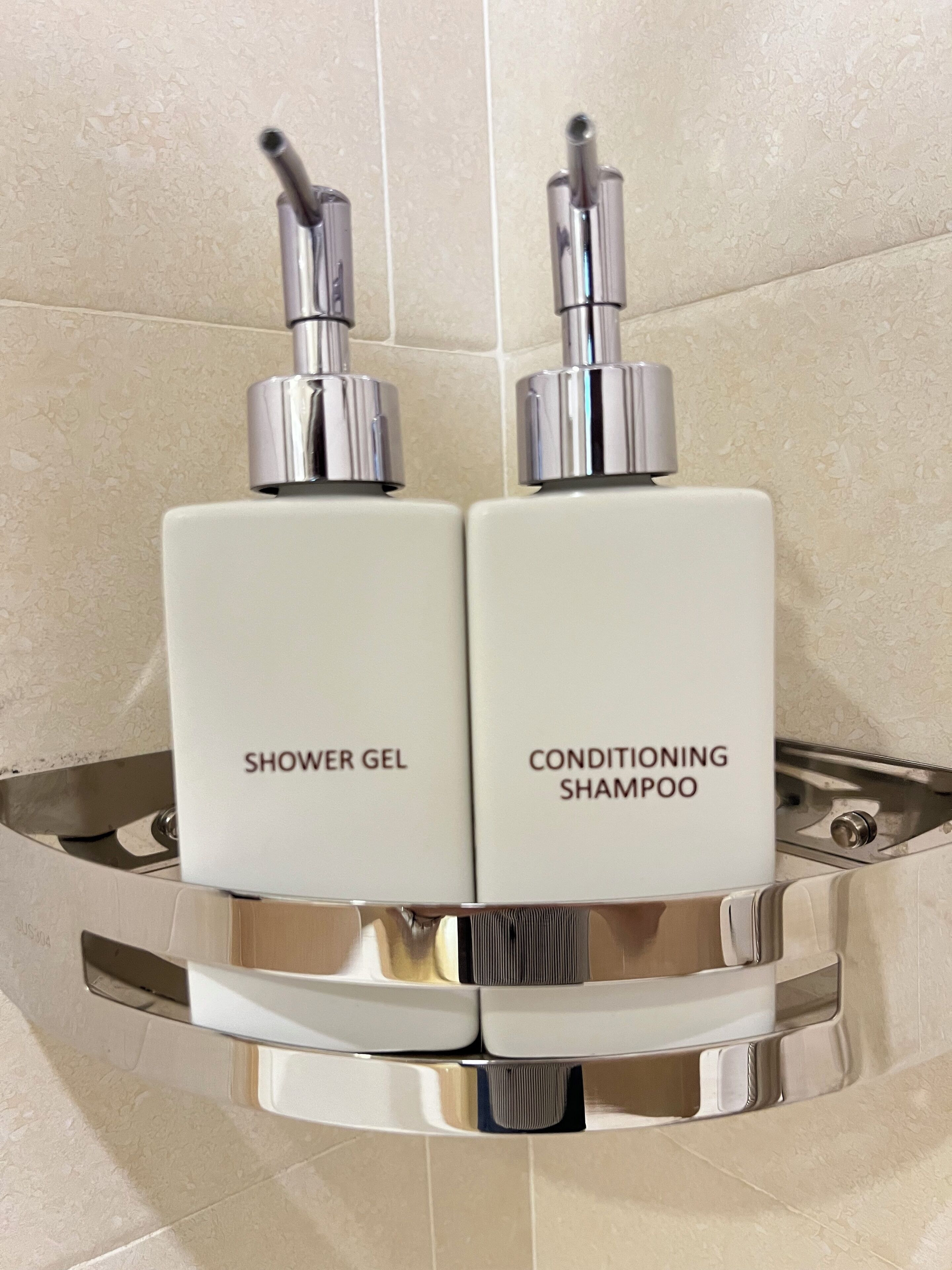 Two bottles of shower gel and conditioning shampoo on a chrome shelf in a bathroom.
