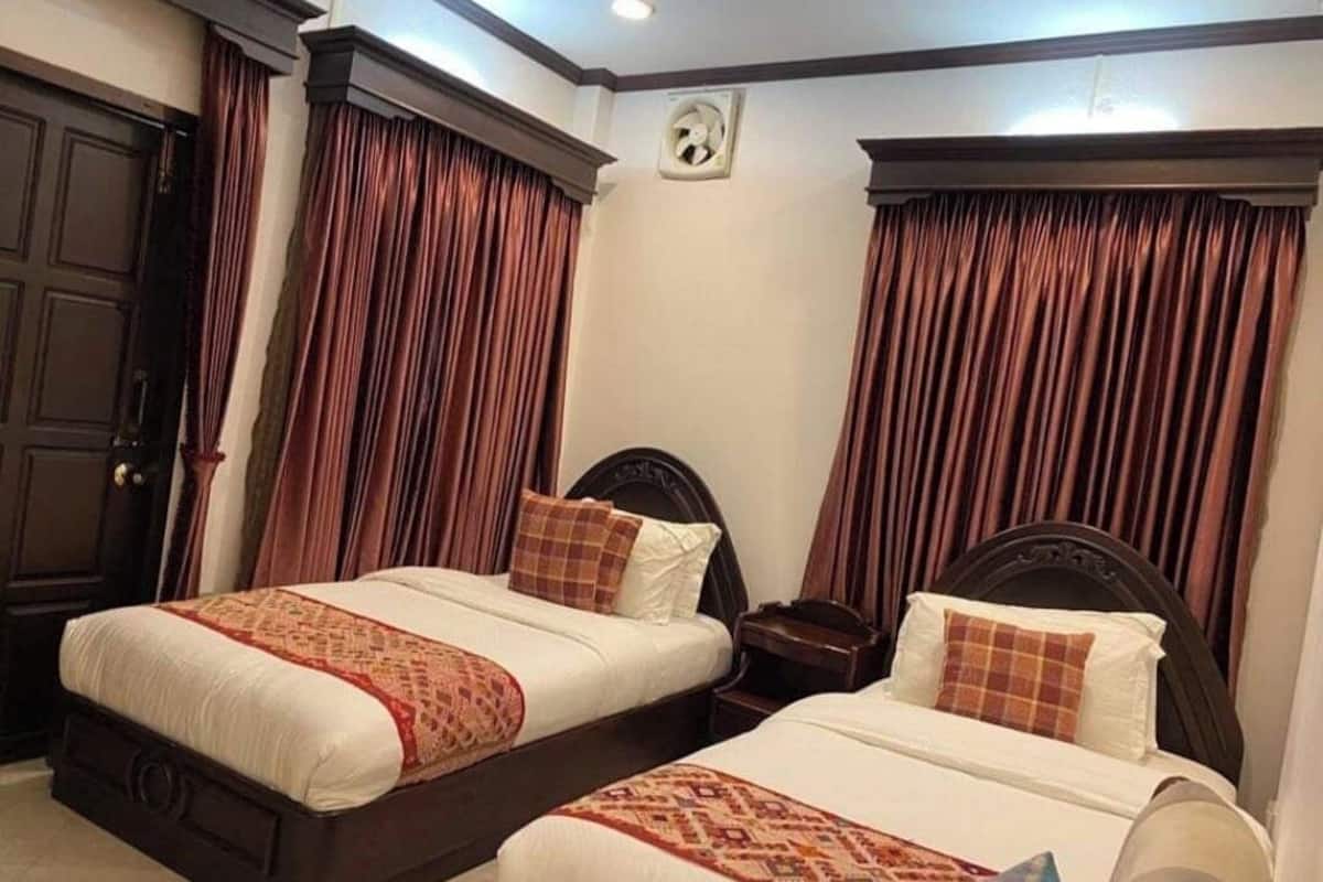 Ein Hotelzimmer mit zwei Betten, dunklen Holz Kopfteilen und braunen Vorhängen.