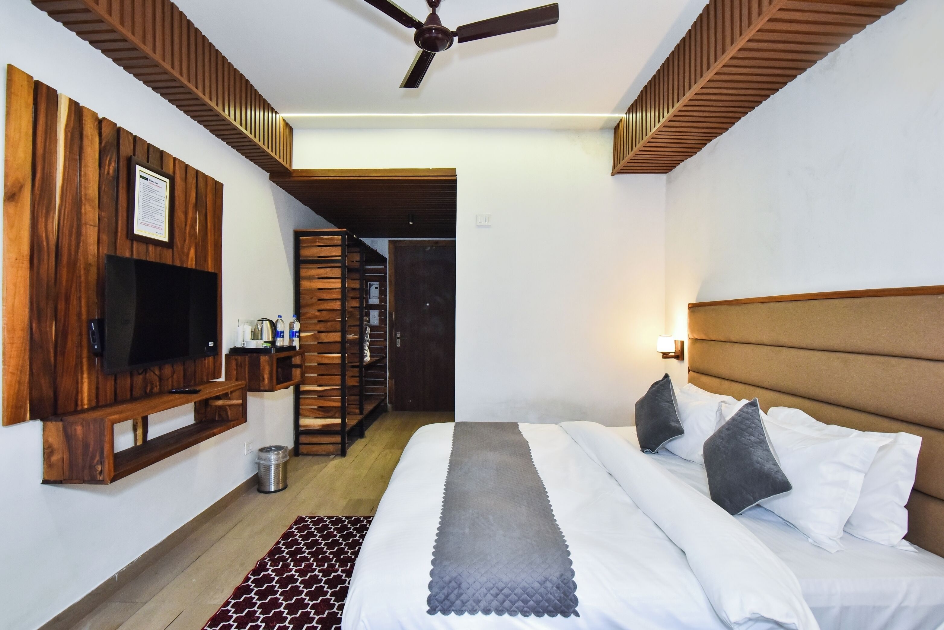 Habitación de hotel con cama, televisión montada en un panel de madera, ventilador de techo y una escalera que conduce a otra habitación.
