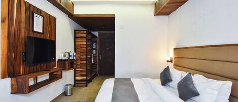 Habitación de hotel con cama, televisión montada en un panel de madera, ventilador de techo y una escalera que conduce a otra habitación.