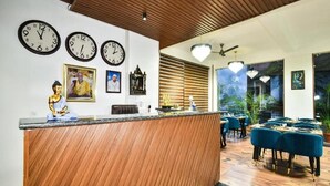 A modern hotel lobby with a wooden reception desk, multiple wall clocks, and a seating area with blue upholstered chairs. - LA Riqueza Koala Inn Mcleod Ganj - Near to Dalai Lama Temple & Mall Road (Dharamshala)
