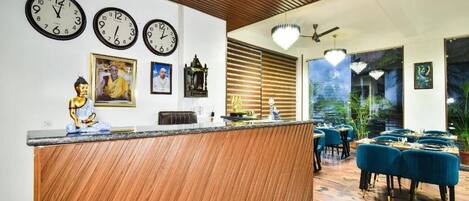 A modern hotel lobby with a wooden reception desk, multiple wall clocks, and a seating area with blue upholstered chairs.