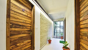 A hallway with wooden doors, a brick wall, and potted plants. - LA Riqueza Koala Inn Mcleod Ganj - Near to Dalai Lama Temple & Mall Road (Dharamshala)